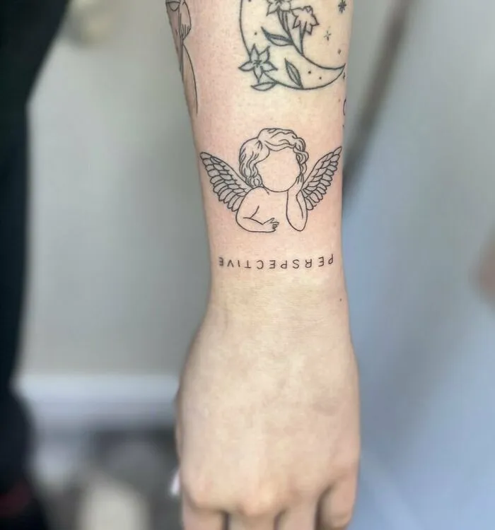 Angel and "PERSPECTIVE" wrist tattoo design, featuring wings and a faceless cherub.