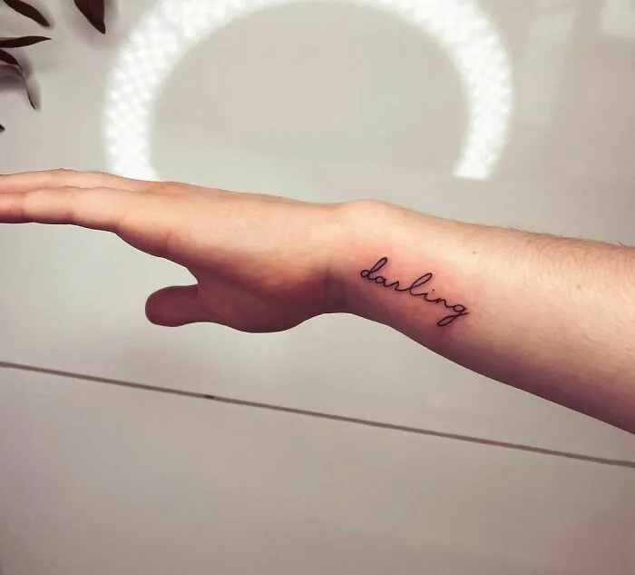 Wrist tattoo design featuring the word "darling" in cursive on a person's arm.