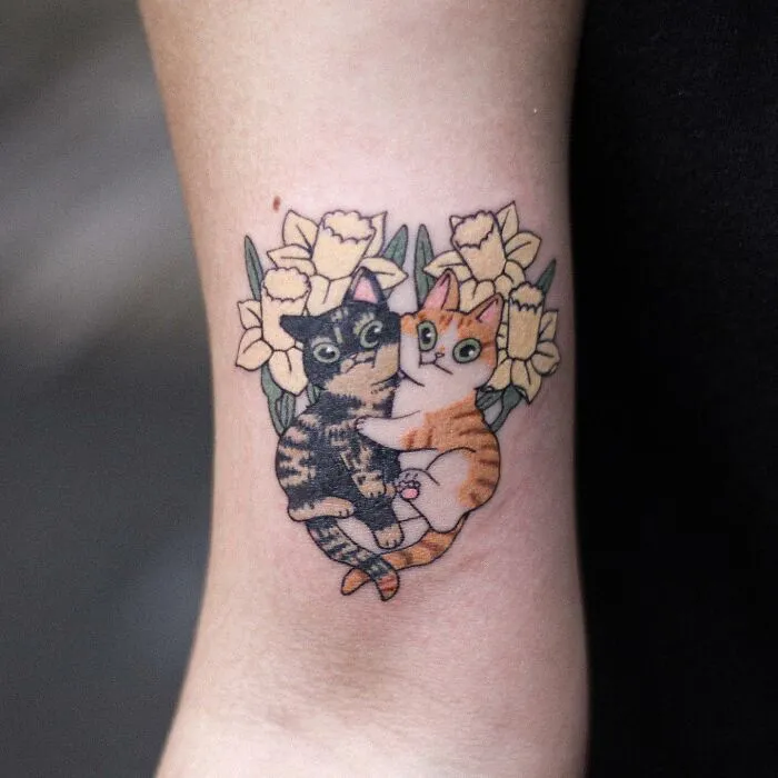 Adorable tattoo featuring two cats surrounded by yellow flowers on skin.