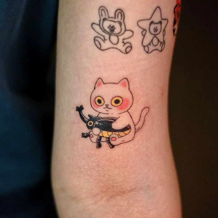 Animal-themed tattoo of a white cat holding a black toy, with other cute designs on the arm.