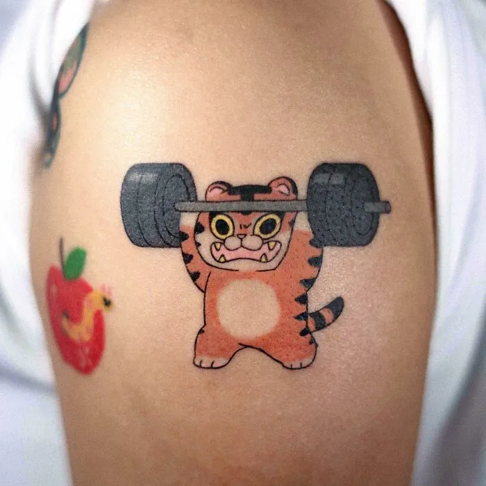 Tattoo of a cartoon tiger lifting weights on skin, showcasing adorable animal-themed art.