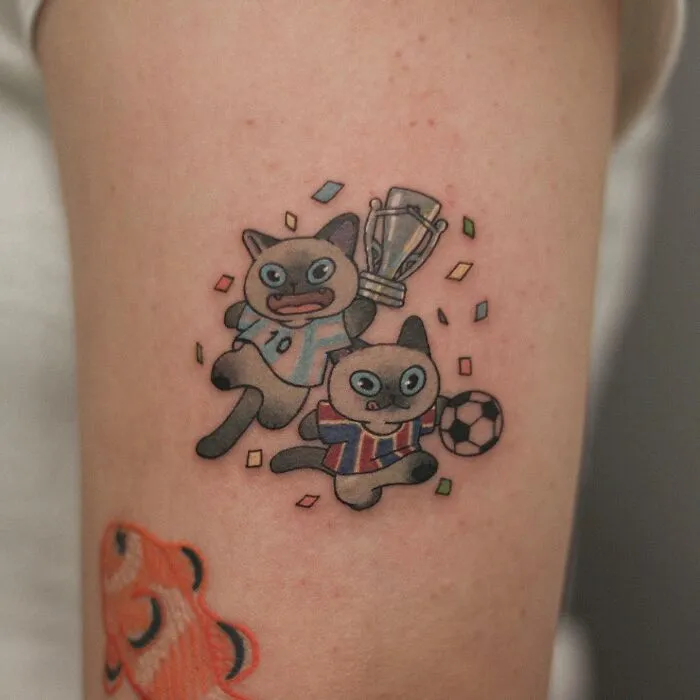 Adorable animal-themed tattoo featuring playful cats with a trophy and soccer ball.