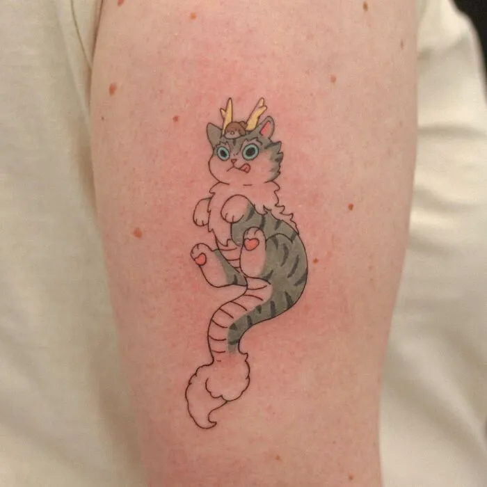 Adorable animal-themed tattoo of a playful cat with a tiny hat on an arm.