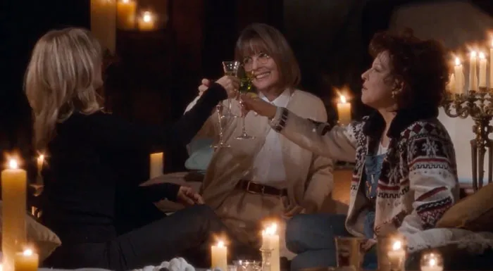 Three women celebrating friendship, toasting with wine glasses in a cozy candle-lit setting.