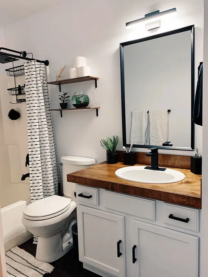 Modern bathroom with wood vanity, black fixtures, and decorative shelves for home decoration inspiration.