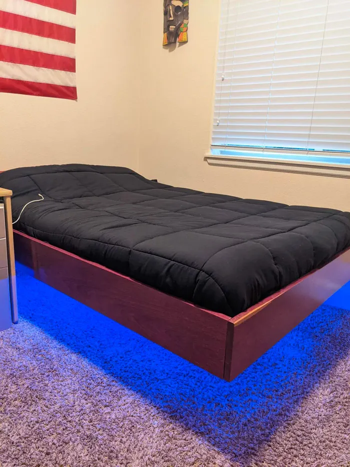 Floating bed with blue LED lights, black bedding adds modern touch to home decoration.