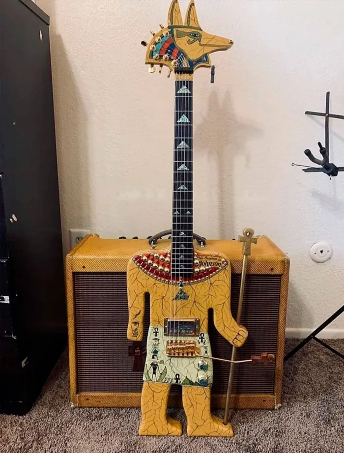 Unusual guitar with an Anubis headstock and Egyptian theme, placed in front of an amplifier.
