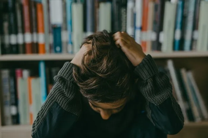 Person sitting with head in hands, expressing emotional distress in a library setting, symbolizing hurtful comments.