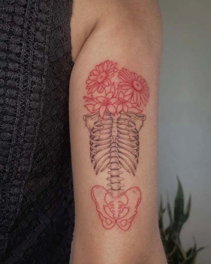 Red ink tattoo of an artistic ribcage with flowers on arm, showcasing a unique design in intricate detail.