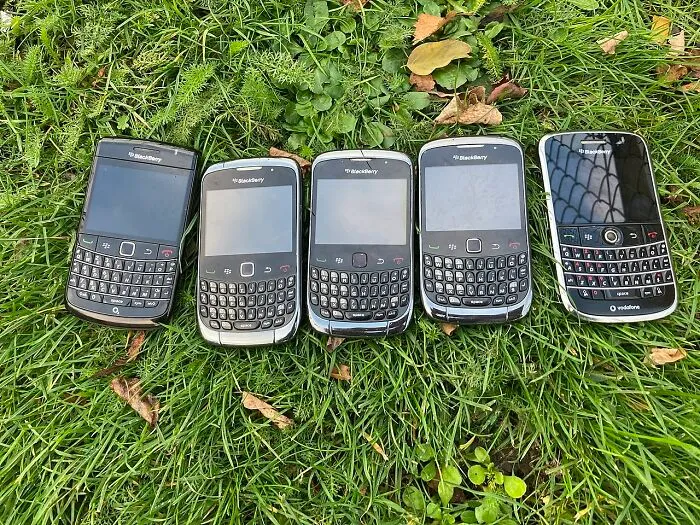 Row of old BlackBerry gadgets with physical keyboards, showcasing classic tech designs popular as trendsetters of their time.