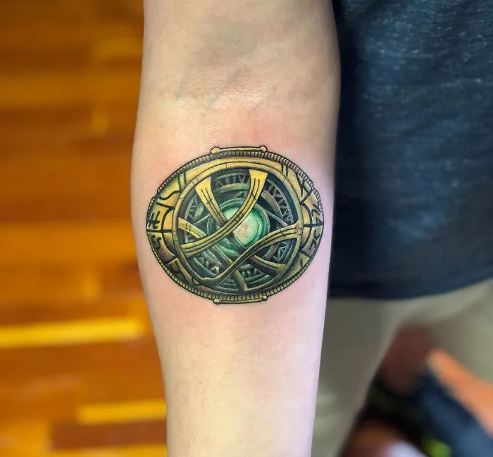 Forearm featuring intricate Marvel tattoo of the Eye of Agamotto, symbolizing mystical powers.
