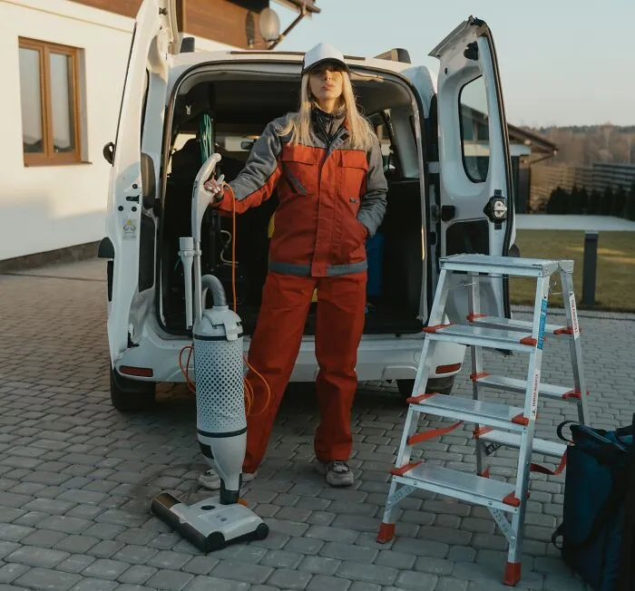 A woman wearing orange suite and holding vacuum cleaner 