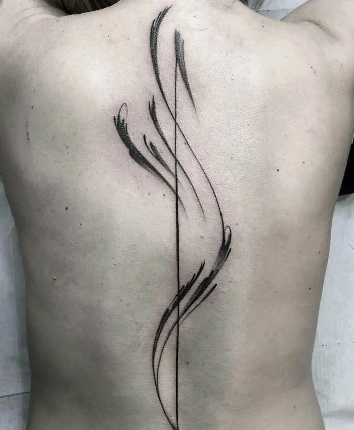 Elegant spine tattoo with abstract, flowing black lines on a person's back.