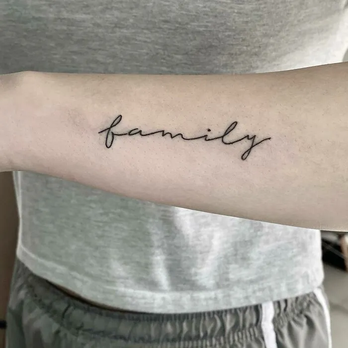 "Family tattoo in cursive script on a forearm, symbolizing unbreakable bonds."