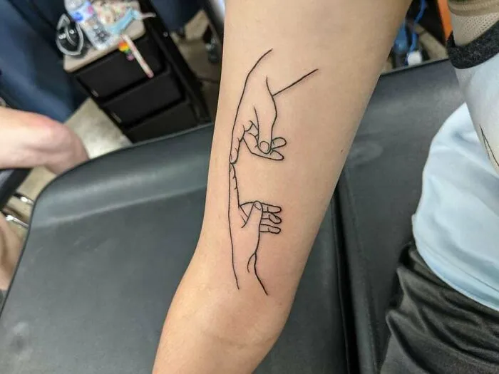 Minimalist family tattoo depicting two hands holding, symbolizing strong unbreakable bonds on a person's forearm.