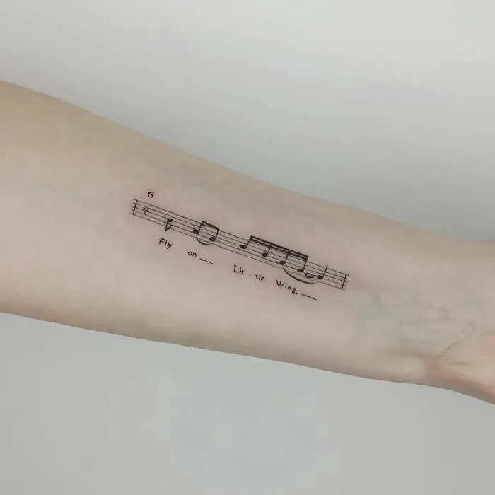 Music tattoo featuring sheet music and lyrics on an arm.