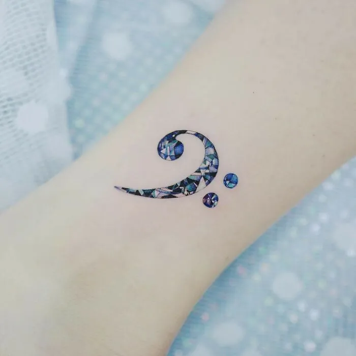 Colorful bass clef music tattoo design on skin.