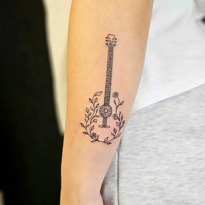 Guitar music tattoo on forearm with floral design, showcasing intricate line art.