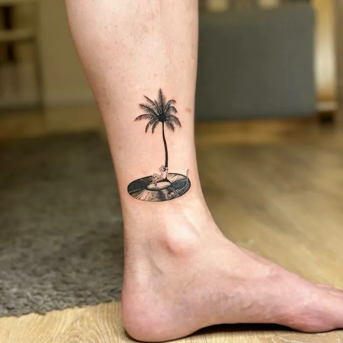 Ankle tattoo featuring a palm tree and vinyl record, representing music tattoos.