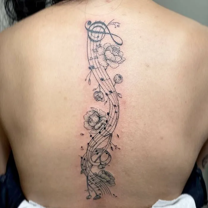 Floral music tattoo design on back featuring musical notes and roses.