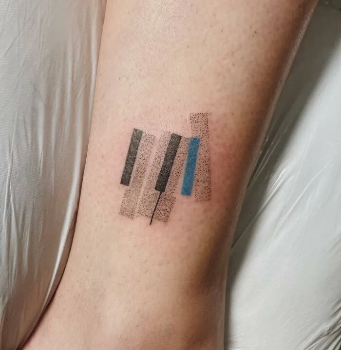 Minimalist music tattoo on a leg featuring abstract piano keys in black and blue.