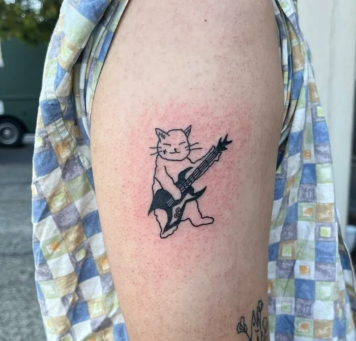 Cat playing guitar tattoo on arm, showcasing unique music tattoo design.