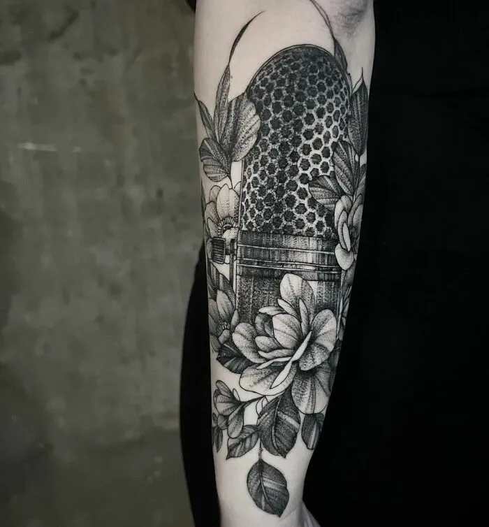 Microphone and floral themed music tattoo on forearm with intricate details.