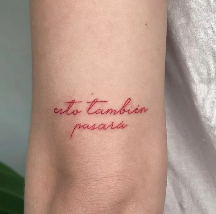 Red ink tattoo on forearm with "esto también pasará" phrase in elegant script.