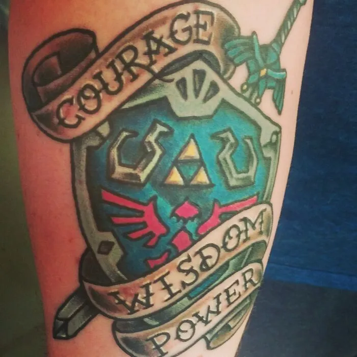 Colorful American traditional tattoo featuring a shield with banners reading "Courage," "Wisdom," "Power."