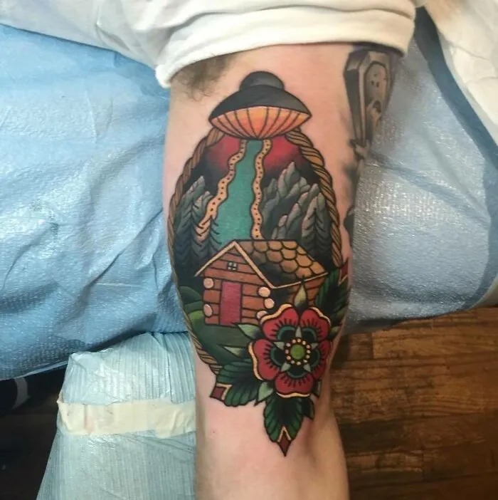 American traditional tattoo of a cabin with UFO and flower design on an arm.