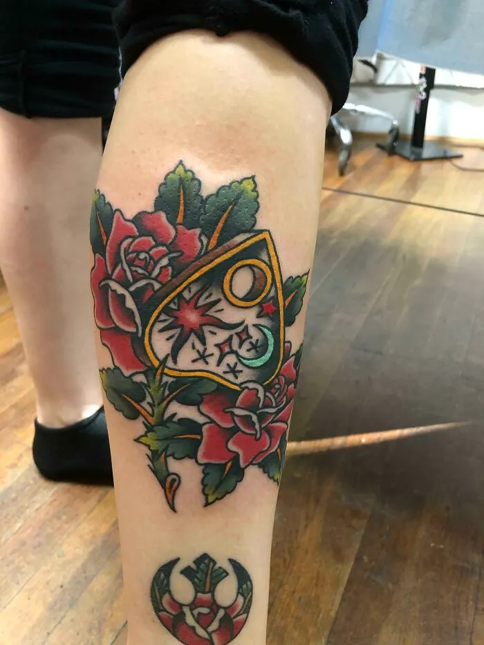American traditional tattoo featuring red roses and a symbolic design on a leg.