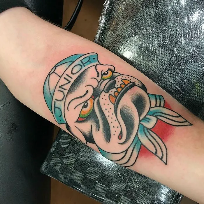 American traditional tattoo of a bulldog wearing a hat and bandana on an arm.