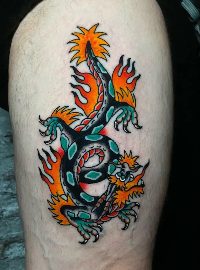 American traditional tattoo featuring a colorful dragon design with flames and bold outlines on the skin.