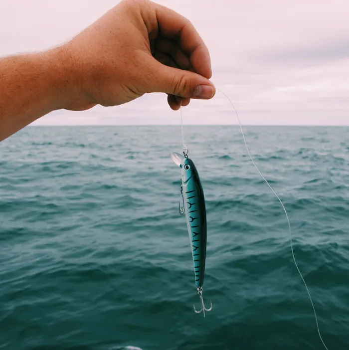Hand holding fishing lure over ocean, illustrating weird hobbies involving fishing.