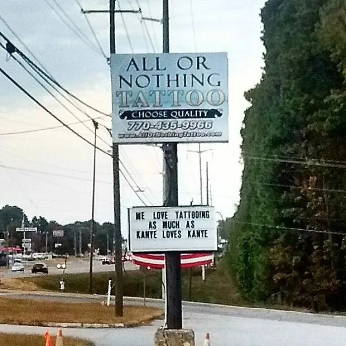 Funny tattoo shop sign on roadside saying, "We love tattooing as much as Kanye loves Kanye".