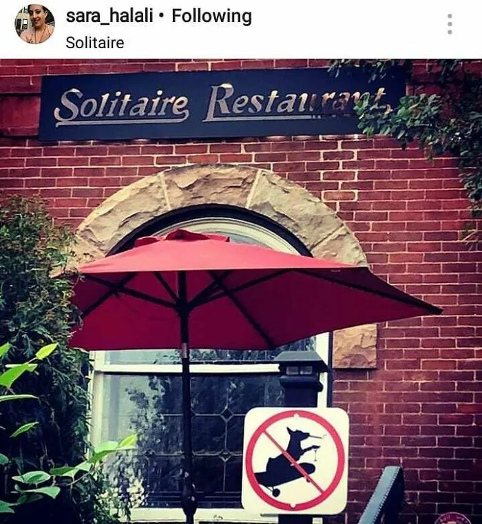 Funny sign at Solitaire Restaurant showing a goat riding a skateboard, placed under a red umbrella.