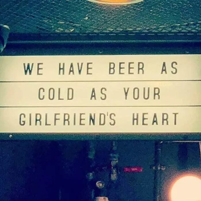 Funny sign in a bar stating, "We have beer as cold as your girlfriend's heart," with humorous wording.
