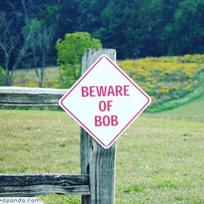 A funny sign reads "Beware of Bob" placed on a wooden fence in a grassy field.