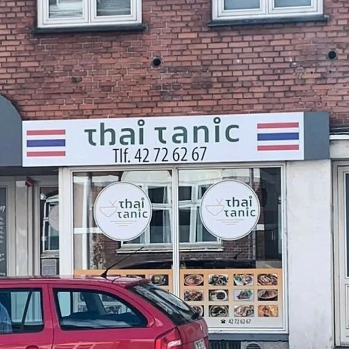 A humorous sign at a restaurant called "Thai Tanic" with flags and a contact number on display.