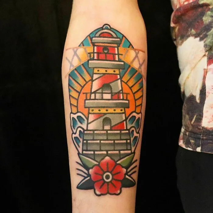 American traditional tattoo of a lighthouse and red flower on forearm, featuring bold colors and classic design elements.