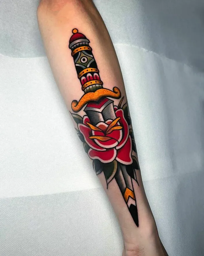 American traditional tattoo of a dagger through a rose, featuring bold colors and classic design on forearm.