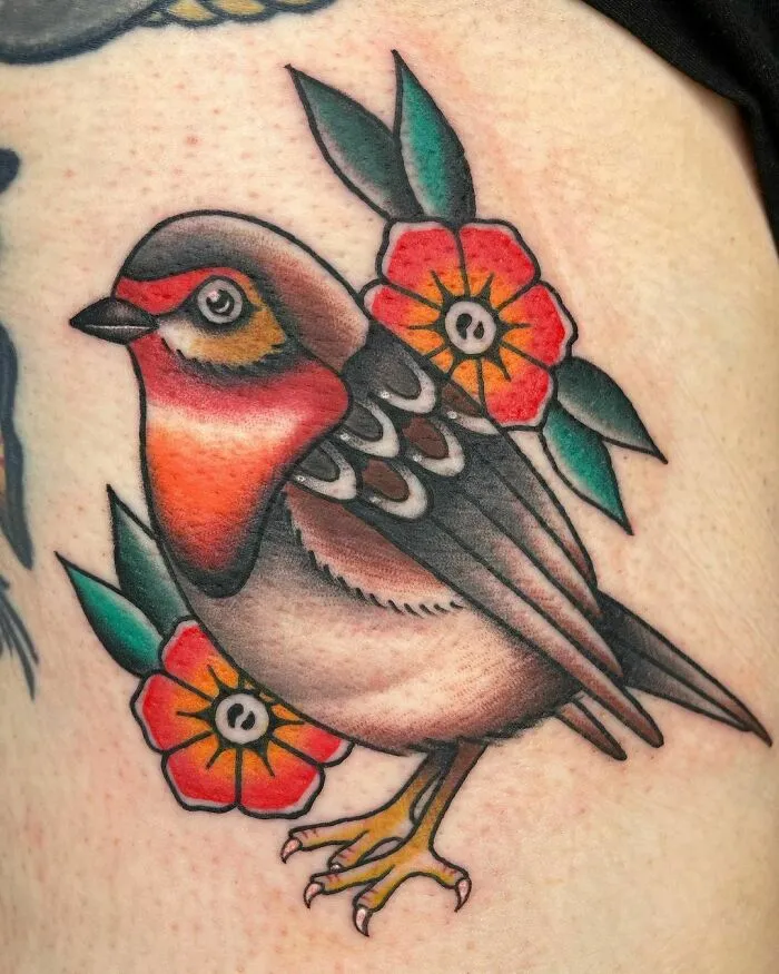 American traditional tattoo featuring a colorful bird with red flowers and green leaves.