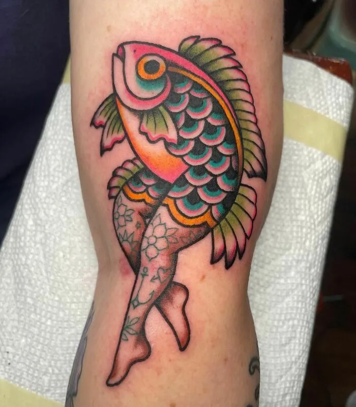American traditional tattoo of a colorful fish with floral-patterned legs on an arm.