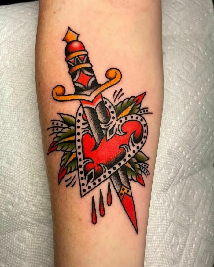 American traditional tattoo with a dagger piercing a heart, featuring bold colors and traditional motifs.