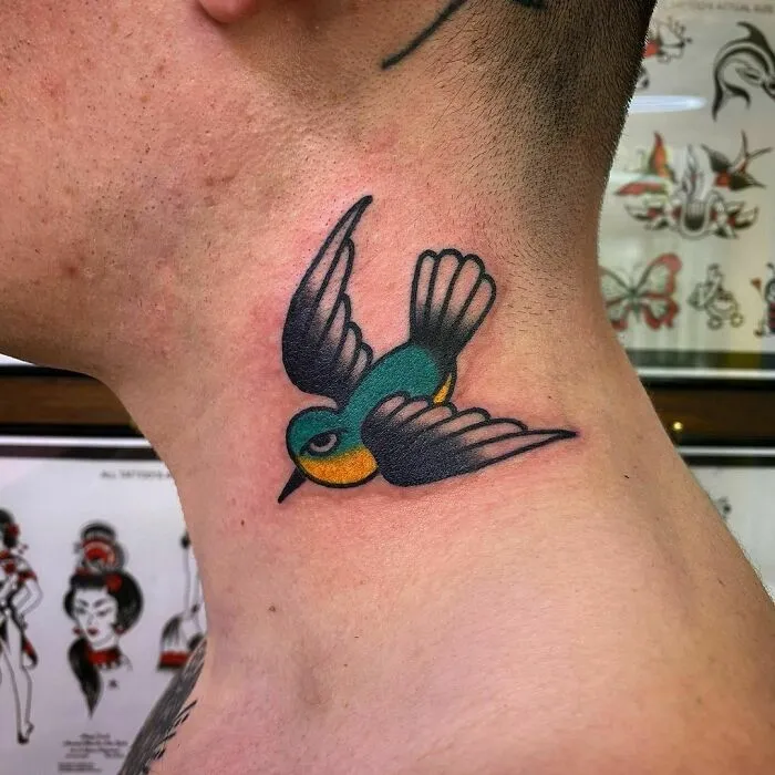 American traditional tattoo of a colorful bird on a person's neck in a tattoo studio setting.