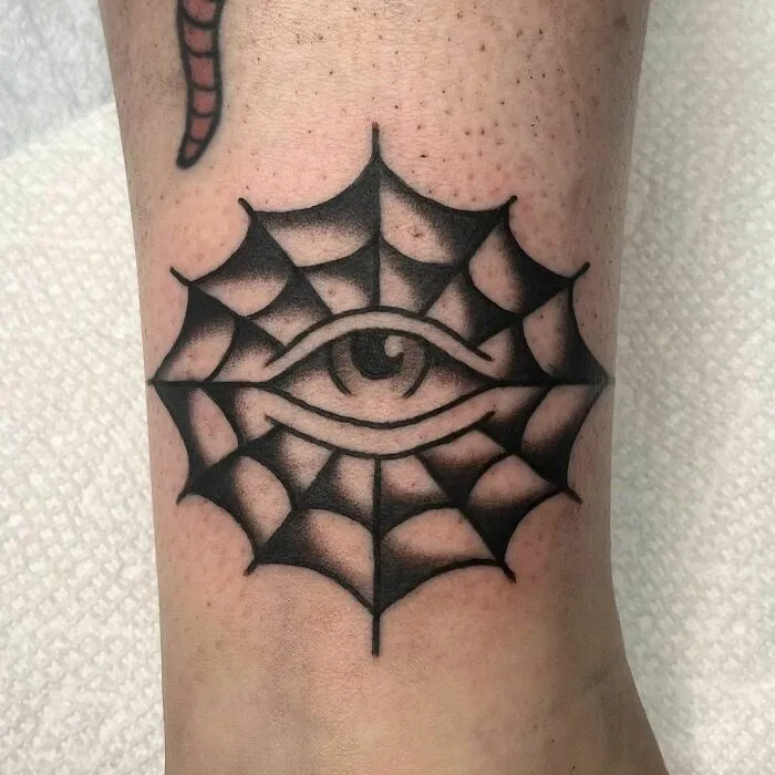 American traditional tattoo featuring an eye within a spiderweb design on forearm.