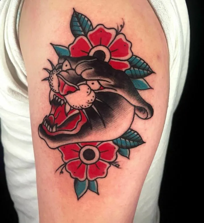 American Traditional tattoo featuring a roaring panther and vibrant red flowers on an arm.