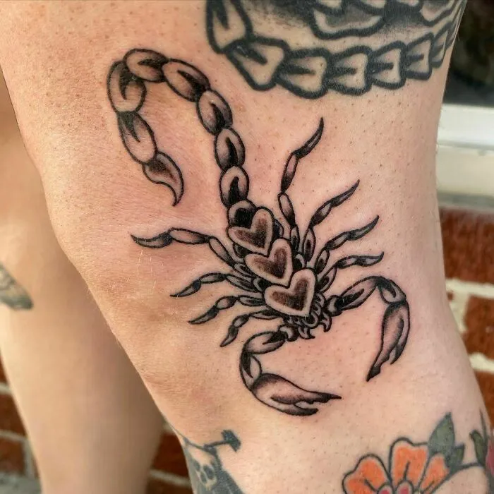 Traditional American scorpion tattoo design with heart motifs on a person's knee.