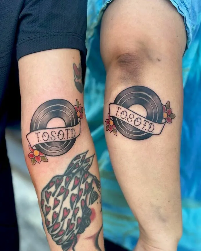 Two arms with American traditional tattoo designs featuring records and floral elements.