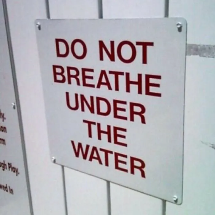 Funny sign reading "Do Not Breathe Under the Water" on a white wall.